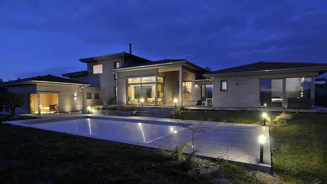 Maison en bois éclairée au crépuscule, avec terrasse et piscine